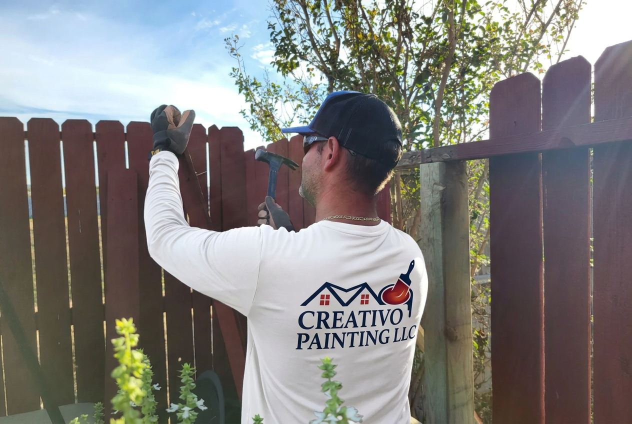 Creativo Painting crew member in a white branded shirt repairing boards on a wood privacy fence
